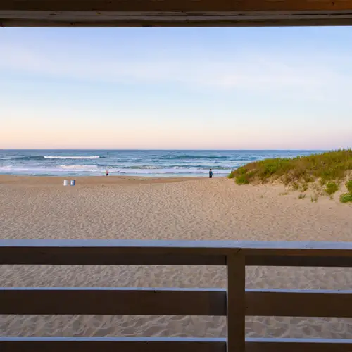 The beach seen through a porch railing at dusk, waves breaking under a pastel sky