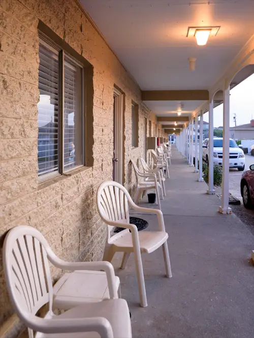 A ground-floor corridor lined with white rocking chairs, lit by a single porch light at dusk