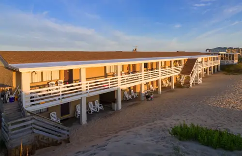 The motel’s long two-storey building directly on the beach, with white railings along both floors and dune grass in the foreground