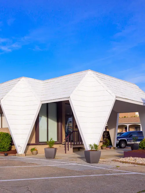 The motel office, a white building with an angular folded roof and a covered walkway to the parking area