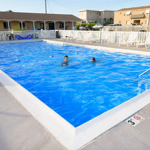 Two guests swimming in the outdoor pool, with the motel building behind it