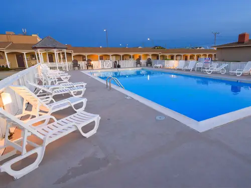 The outdoor pool at dusk, white loungers around its edge and the pool lights just coming on