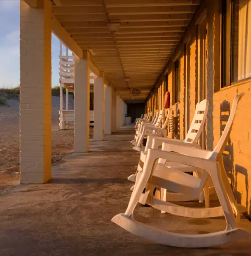 A row of white rocking chairs on the covered ground-floor porch, lit by late-afternoon sun